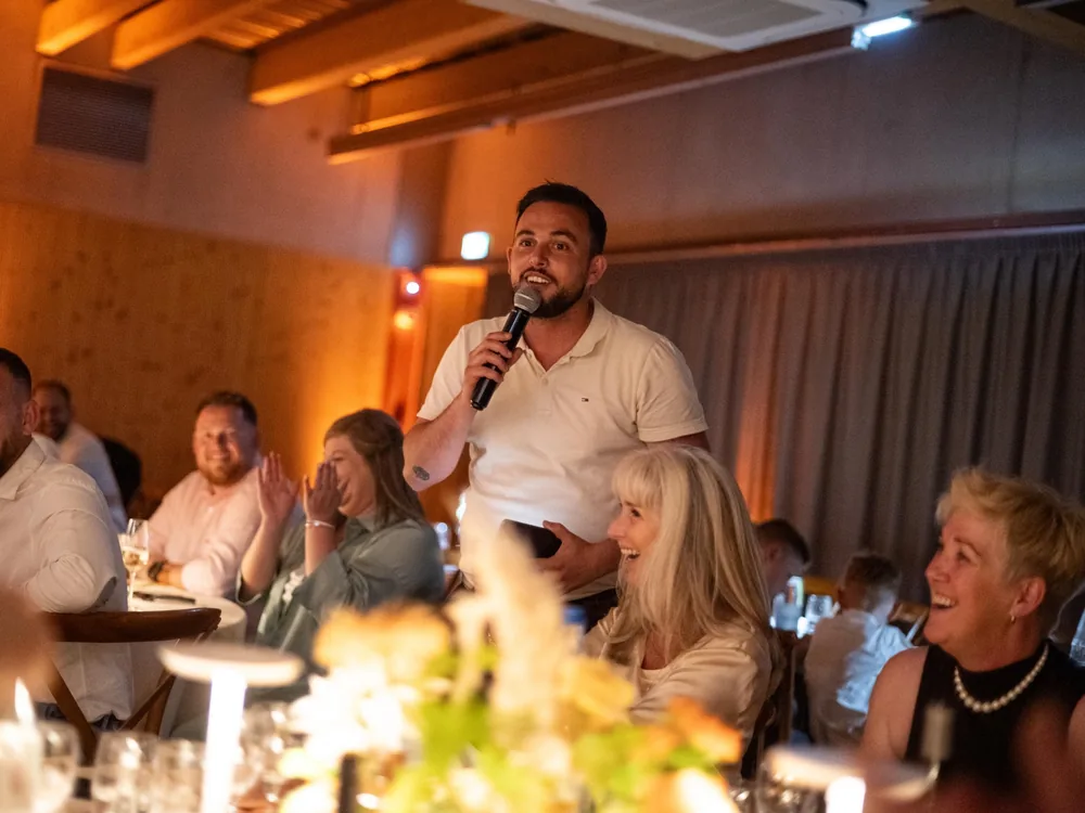 Thibaut Salvador au micro entre les tables, invités hilares pendant une soirée privée